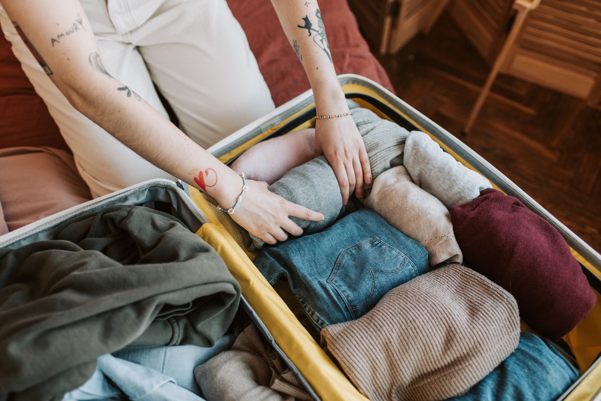 Close-up of a person packing various clothing items into a suitcase, ready for travel.